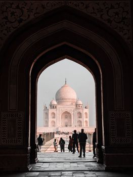 Silhouette of people in front of the Taj Mahal viewed through an ornate archway.