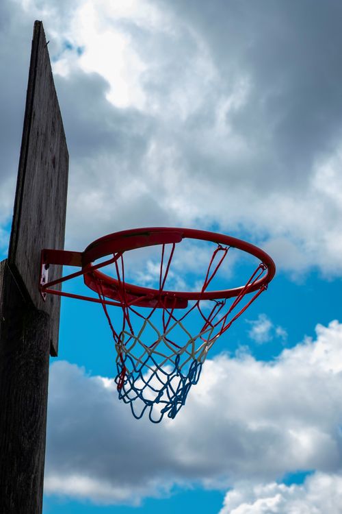 Free Close-up view of a basketball hoop with net against a bright cloudy sky, ideal for sports themes. Stock Photo
