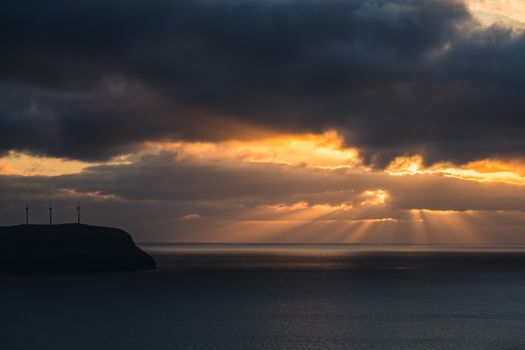 Sunrise illuminating ocean waters with dramatic clouds and sunbeams.