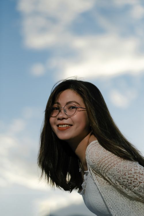 Free Portrait of a smiling woman in eyeglasses posing outdoors under a clear sky. Stock Photo