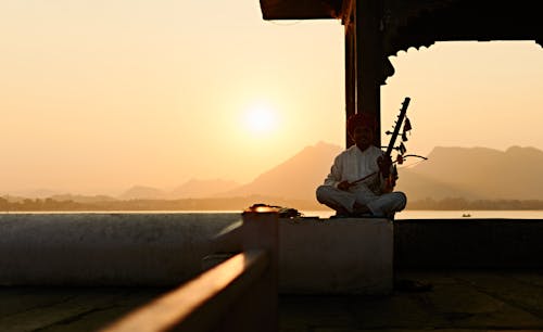 Man in Traditional Clothing Sitting on Wall at Sunset