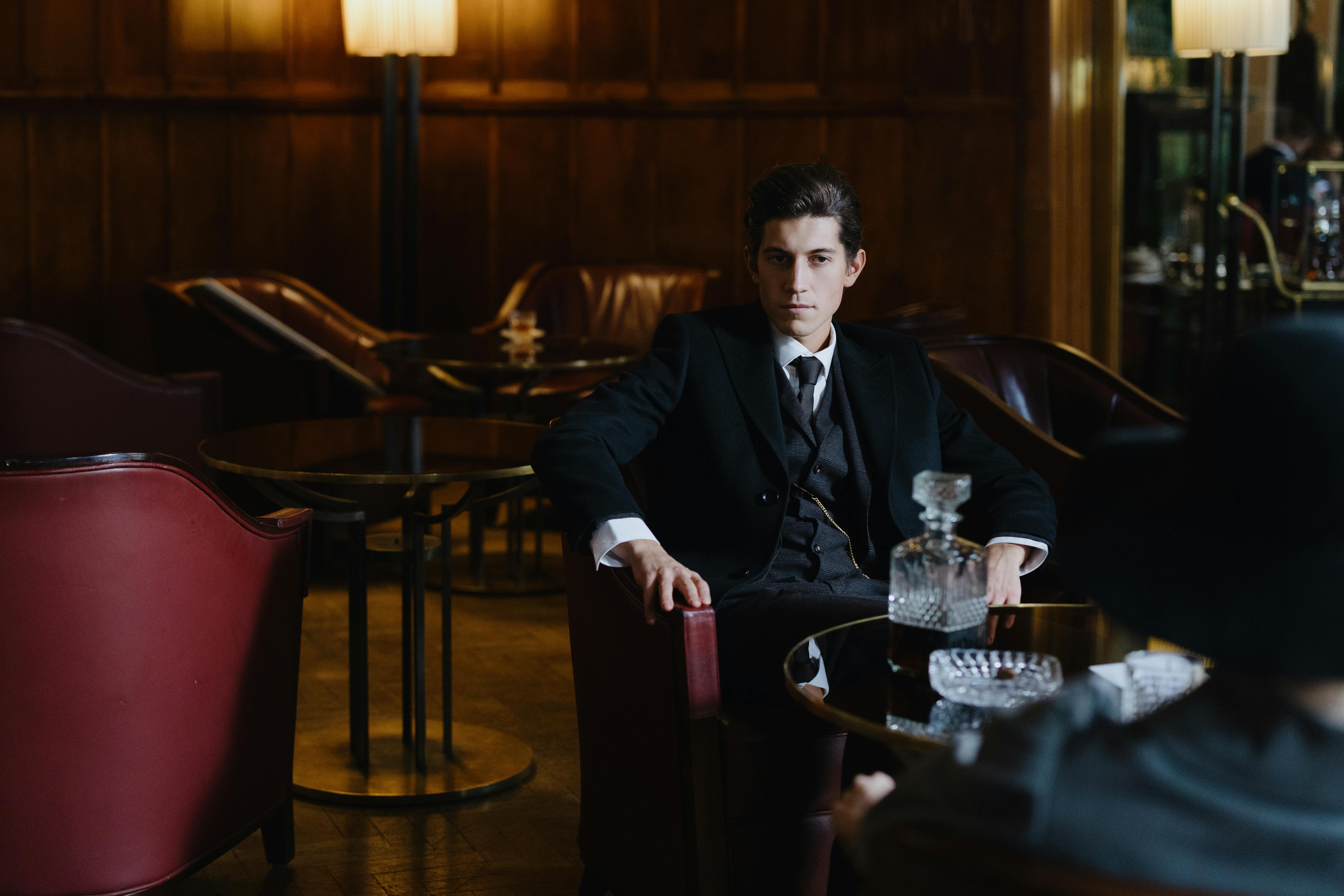 Sophisticated man in a suit seated in a vintage lounge setting, exuding elegance and style.