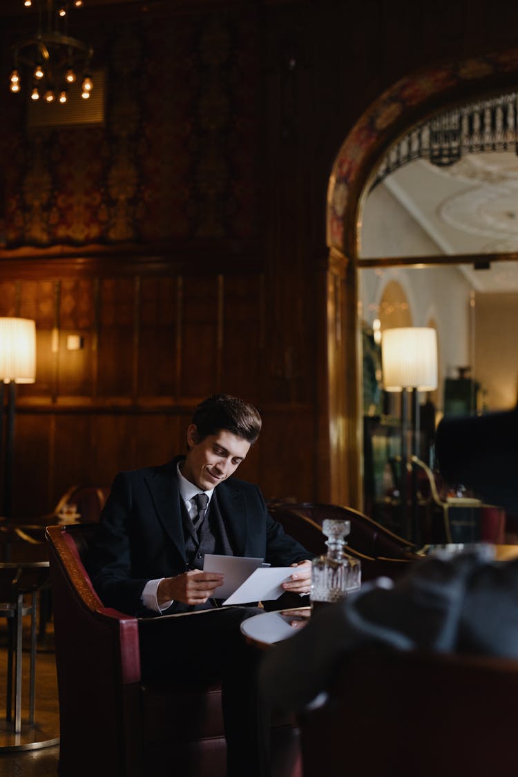 A Man In Black Suit Sitting On Chair Holding Papers