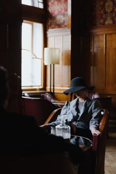 Woman sitting in vintage restaurant, wearing retro style gray dress and broad brim hat.