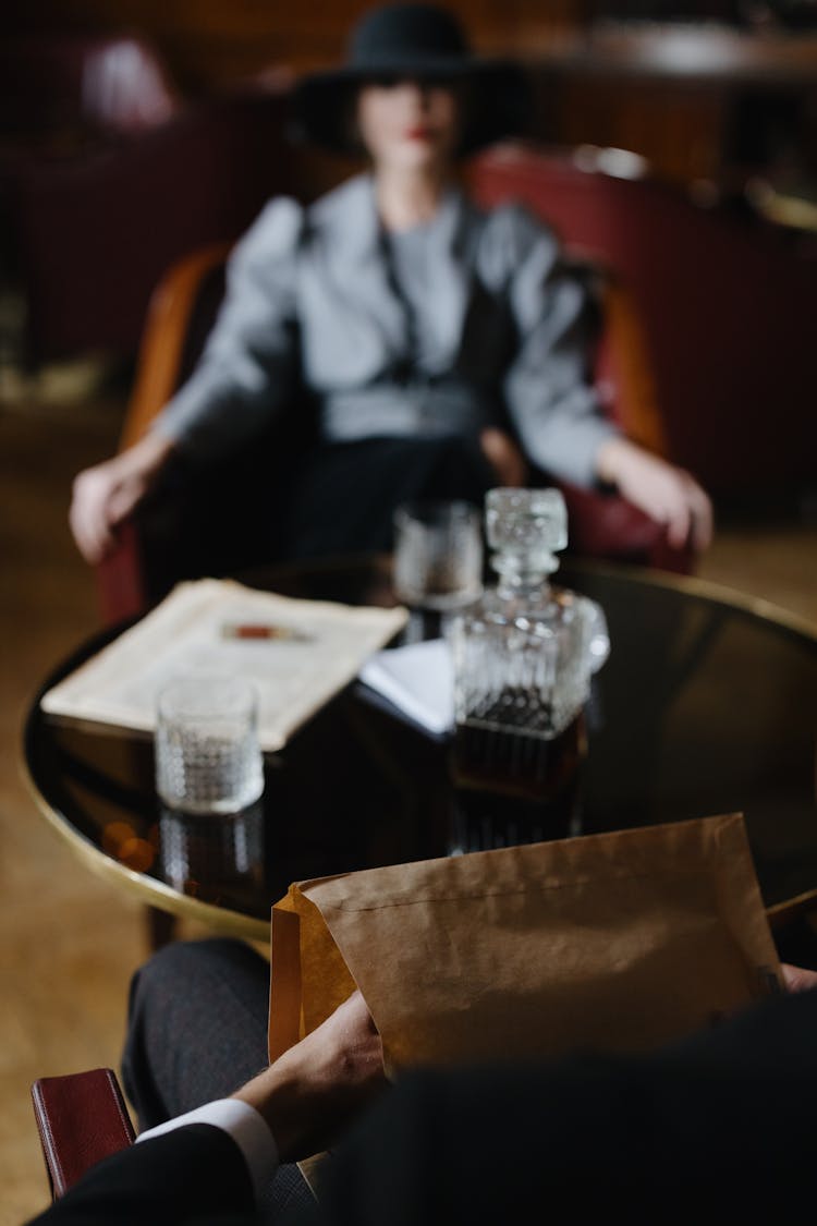 A Person Holding Brown Envelope Across A Person Wearing Black Hat