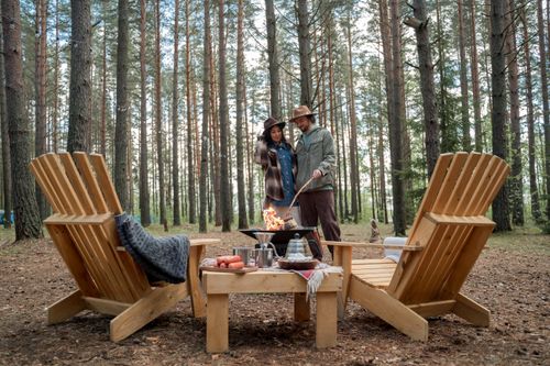 Free Couple enjoys a cozy campfire among wooden chairs in a serene forest setting. Stock Photo