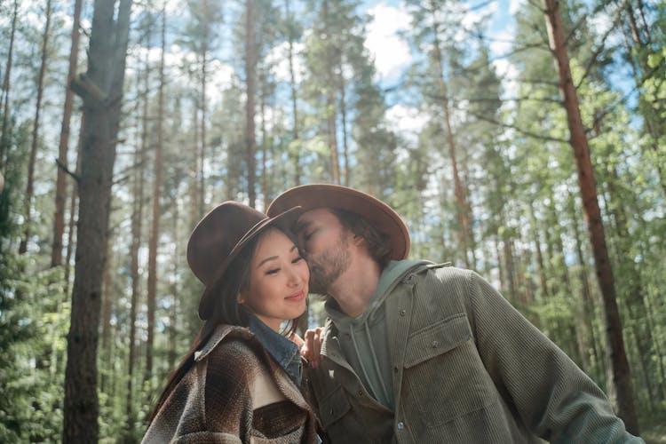 A Man Kissing A Woman On The Cheek In The Woods