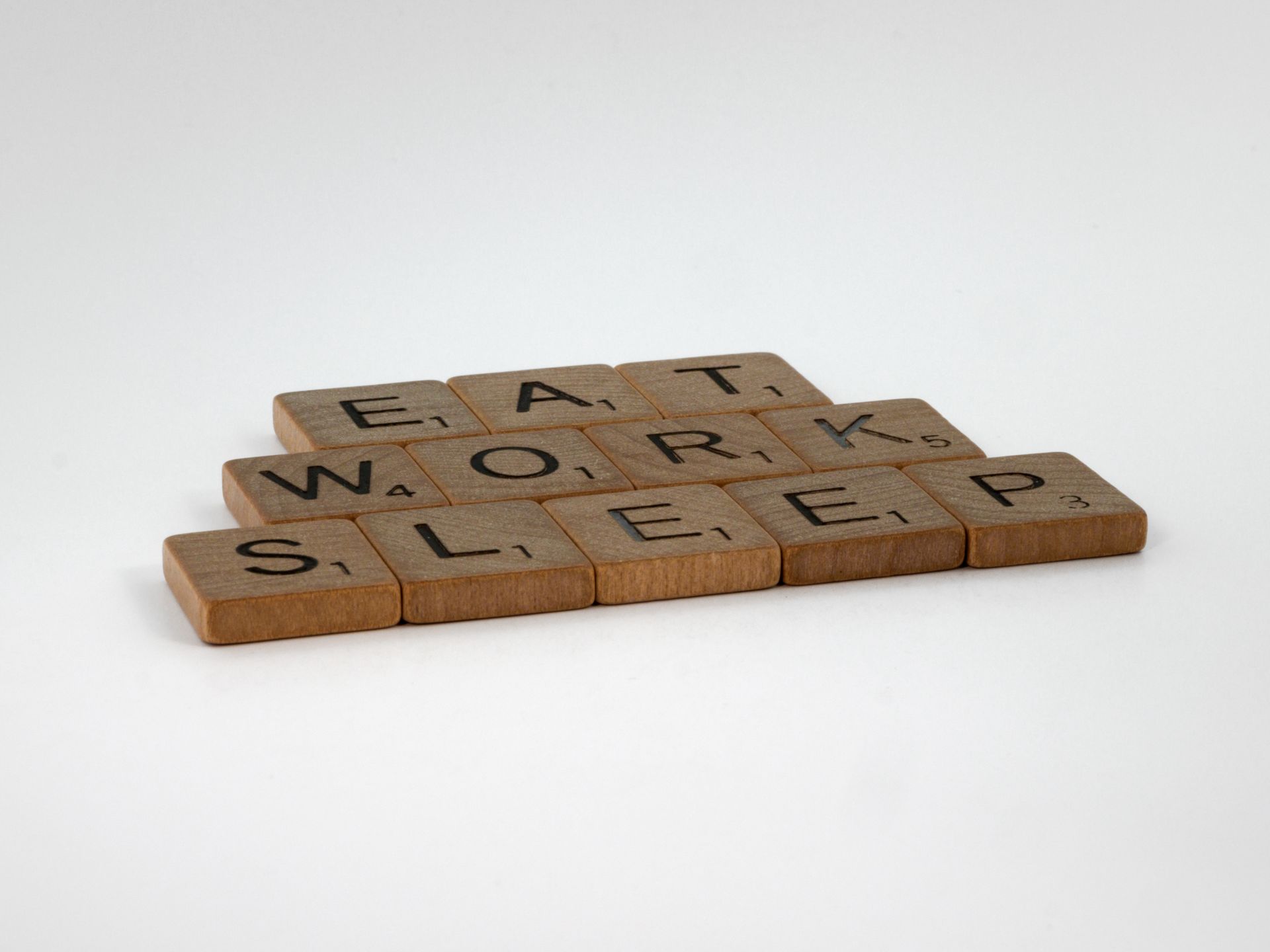Wooden letter tiles forming the words 'Eat Work Sleep' on a white background.