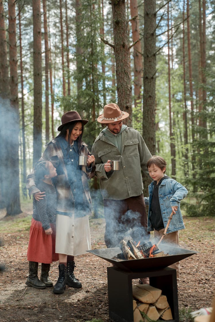 A Happy Family Standing By A Firepit In The Woods