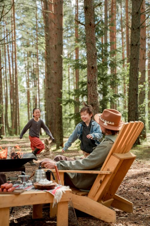 Free Joyful family camping scene with kids playing near a bonfire in a pine forest. Stock Photo