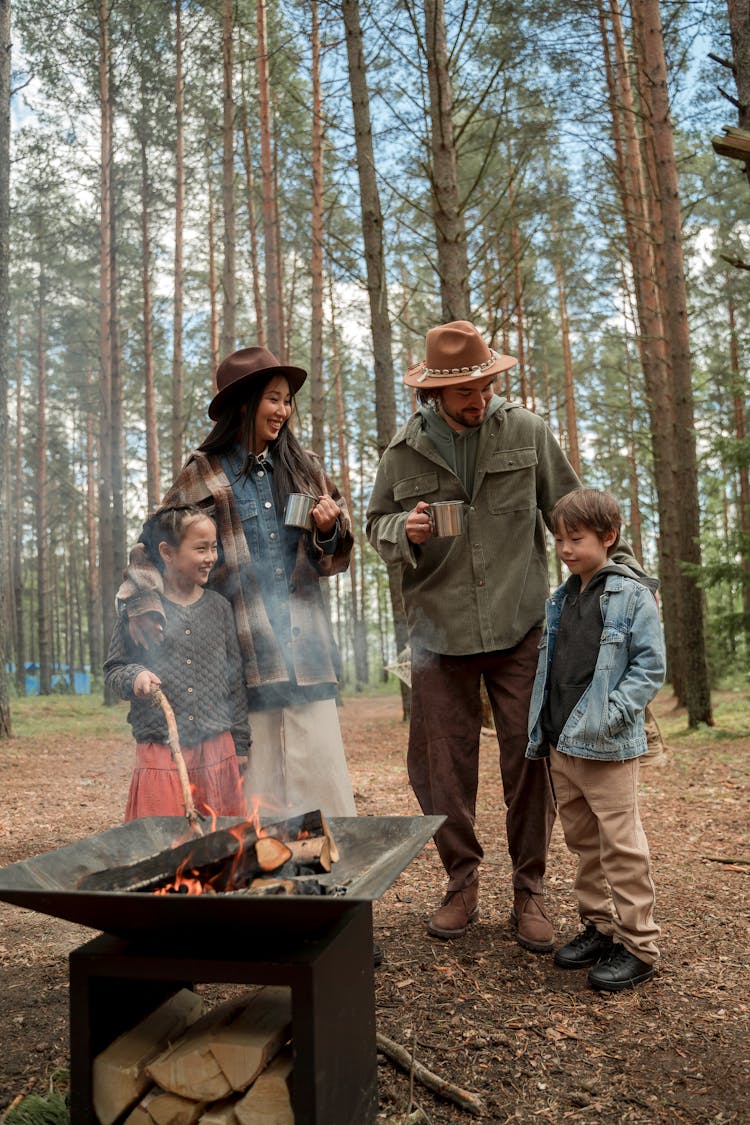 A Happy Family Standing By A Firepit In The Woods