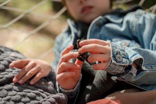 Free Close-up view of a child lying outdoors holding a pine cone with soft focus. Stock Photo