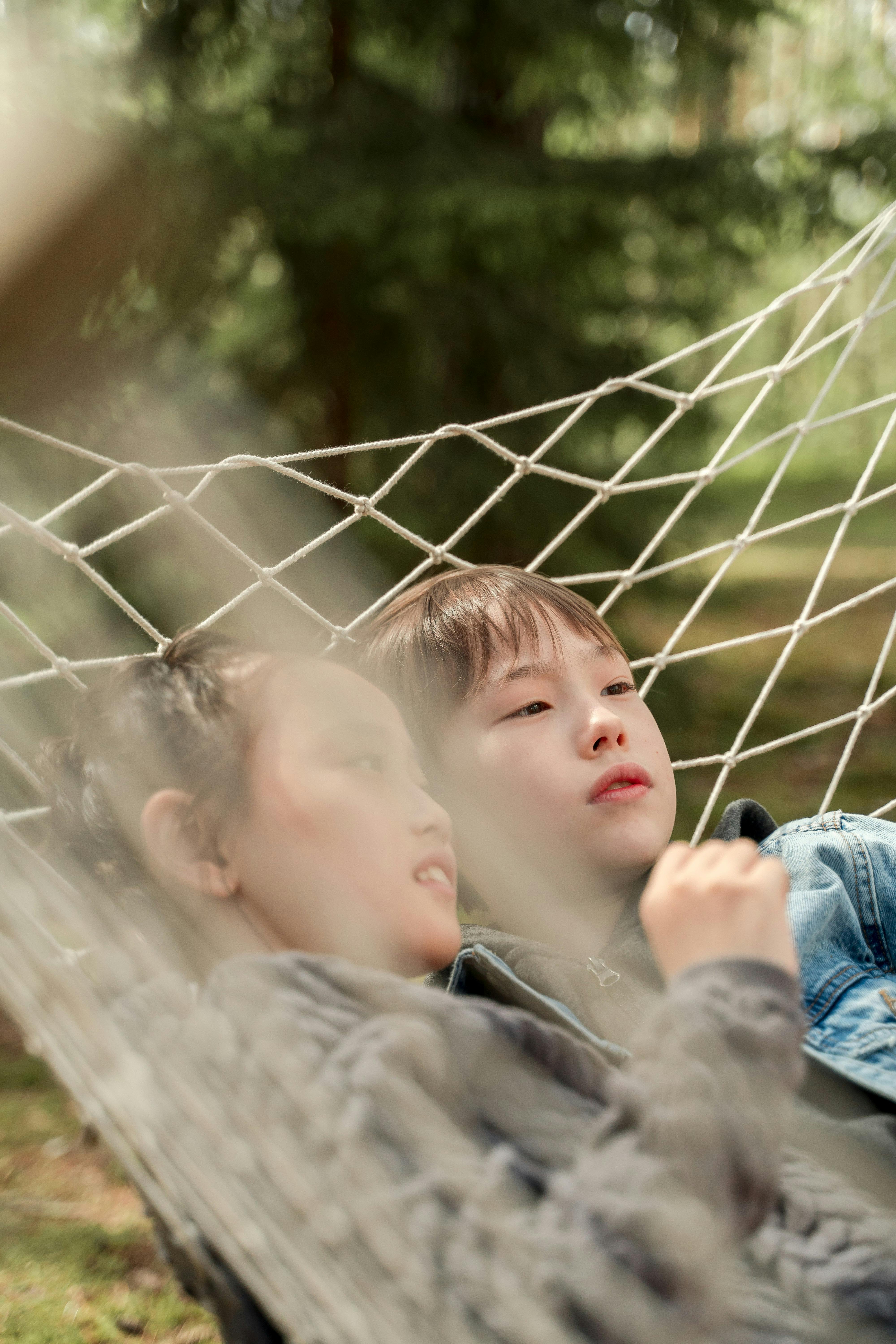 Young siblings relaxing in a hammock outdoors amidst lush greenery.