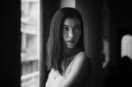 Black and White Photo of a Woman Posing by a Window