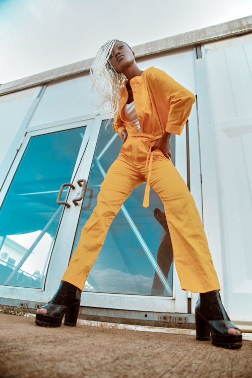 Woman in Yellow Jumpsuit Standing Beside Glass Doors