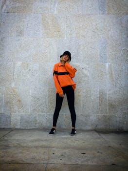 Stylish woman posing in an orange outfit against a stone wall, showcasing urban fashion.