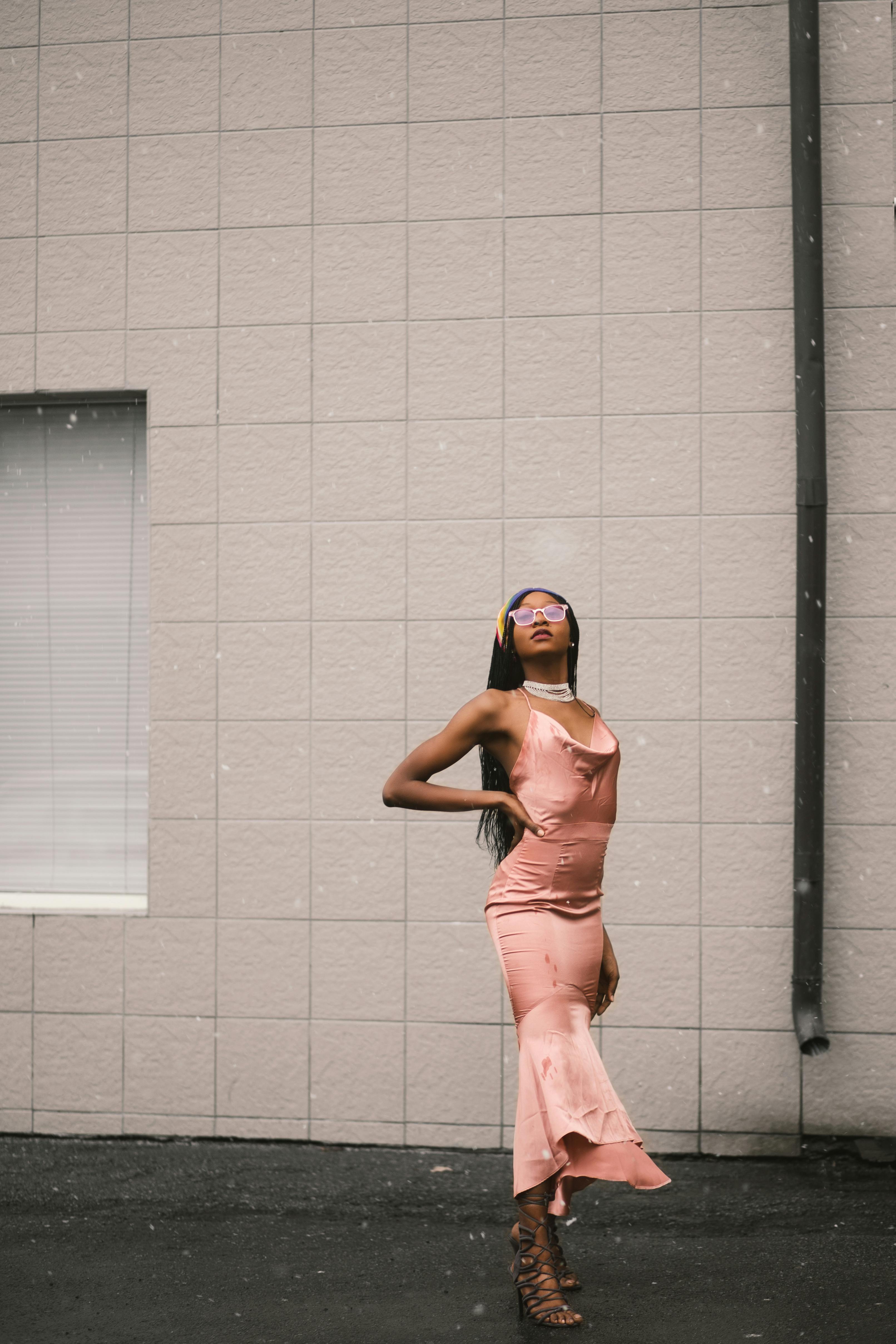 Stylish woman posing in pink dress against textured wall, exuding confidence.