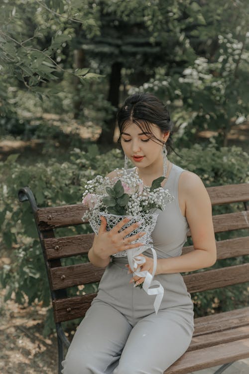 Woman Tank Top Holding Bouquet of Flowers Sitting on Brown Wooden Bench