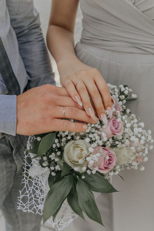 Free Close-up of a couple's hands with wedding rings over a beautiful bouquet, symbolizing love and unity. Stock Photo