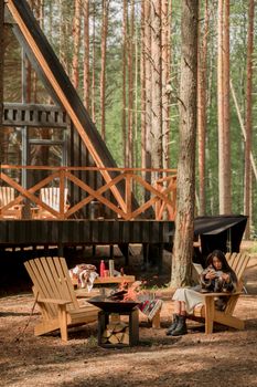 Woman relaxing by a firepit at a rustic cabin in a serene forest setting.