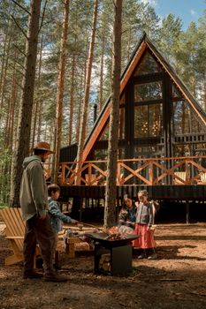 A family gathering around a campfire outside a rustic A-frame cabin in a forest setting, creating warmth and bonding.