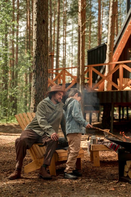 Free A father and son bond by the campfire at a forest cabin, sharing a tranquil outdoor moment. Stock Photo