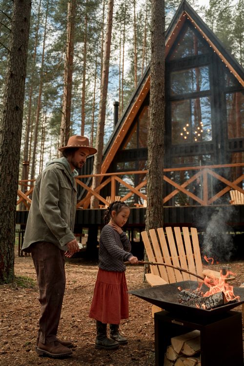 Free A father and daughter bonding over a campfire near a cozy A-frame cabin in the woods. Stock Photo