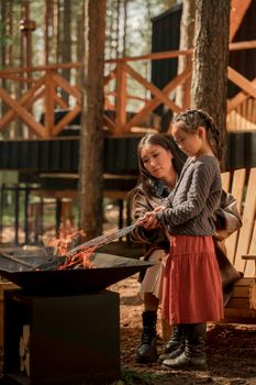 A mother and daughter enjoy quality time at a cozy outdoor campfire in a forest setting.