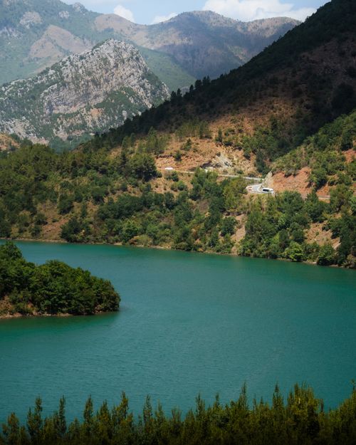 Free A calm mountain lake surrounded by dense green forest and rocky hills under a clear sky. Stock Photo