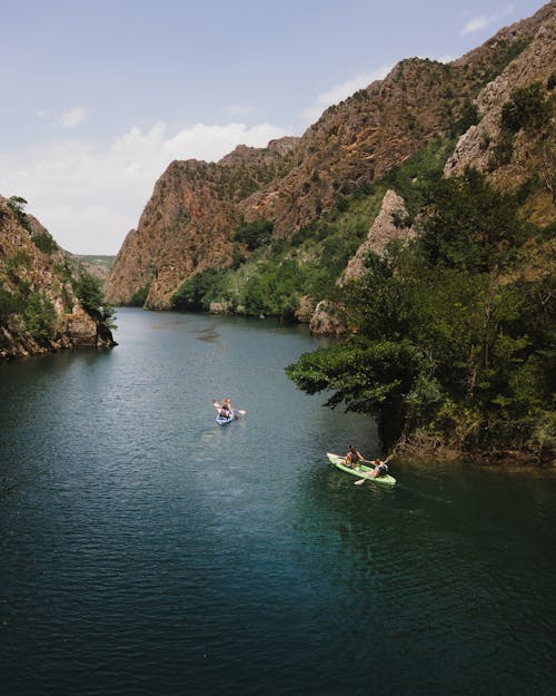 People Riding Kayaks on River Between Green Mountains