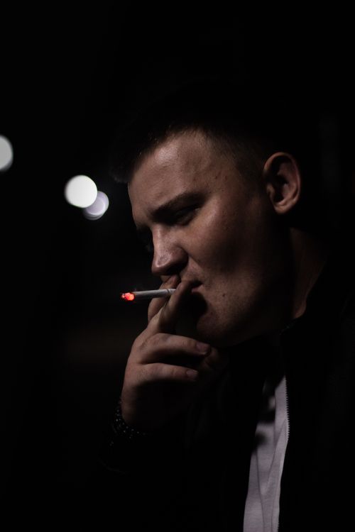 Free A contemplative man smoking a cigarette in a dark ambiance. Stock Photo