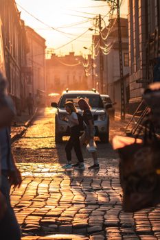 People crossing a cobblestone street during a vibrant sunset, creating a warm atmosphere.