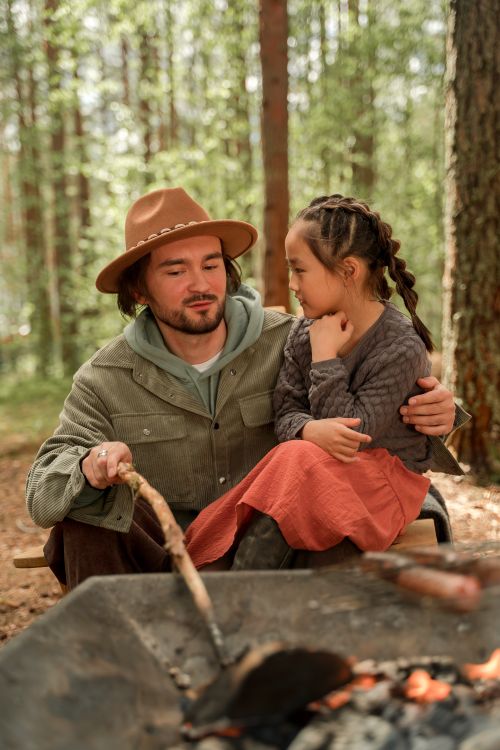 Free A man and his daughter bond by the campfire in a serene forest setting. Stock Photo