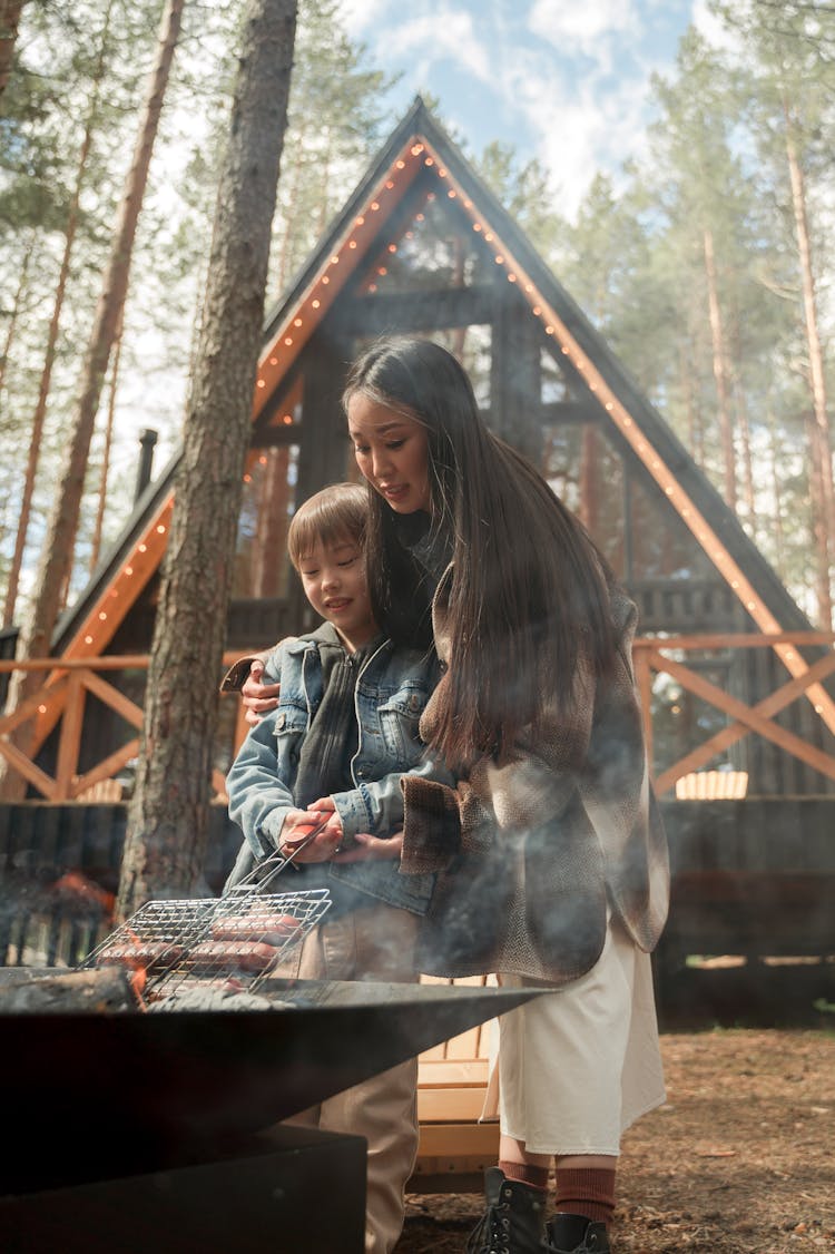 A Woman And Kid Grilling Sausages On A Fire Pit