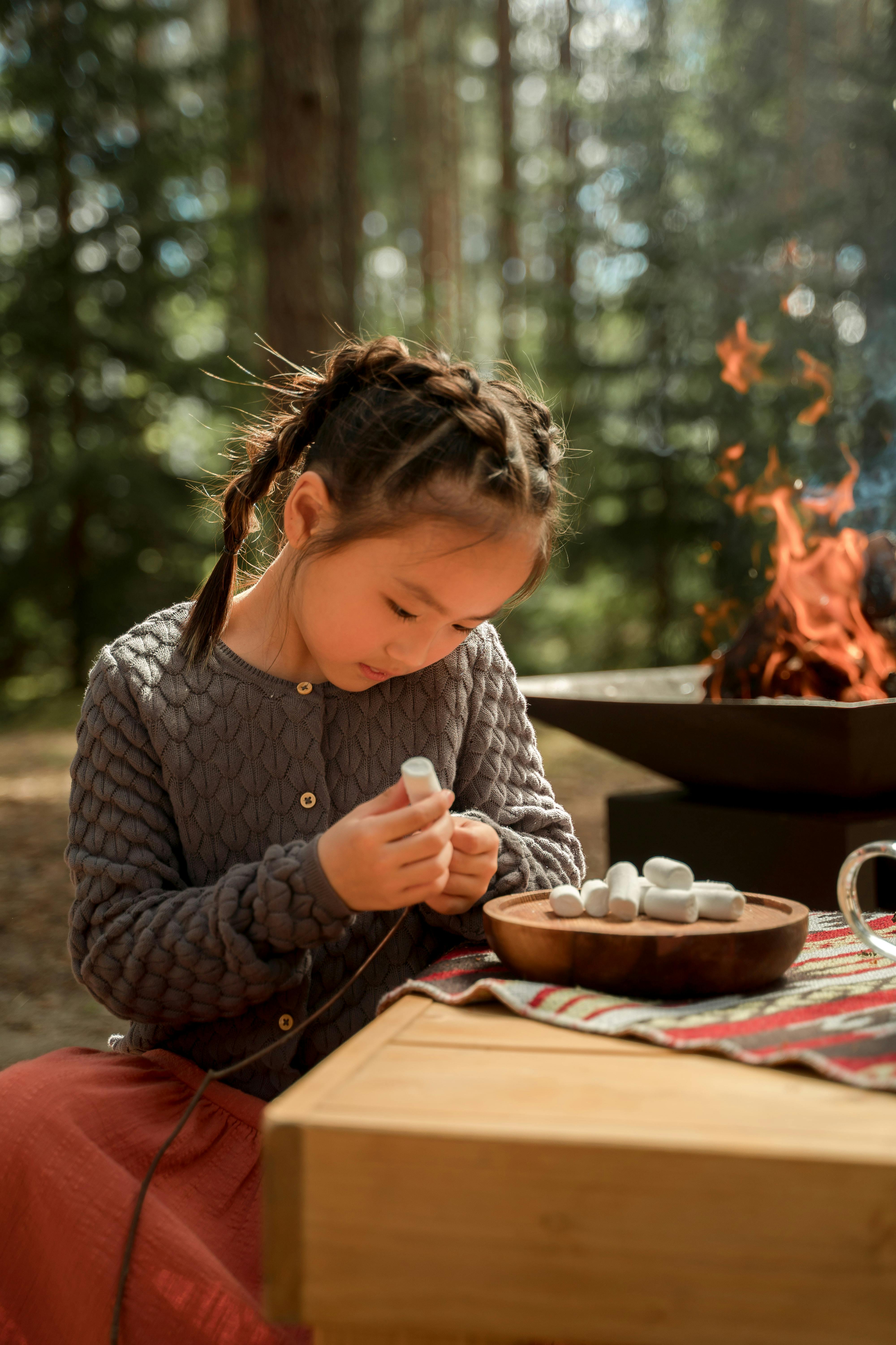 a girl skewing a marshmallow in a stick