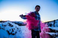 日落时分，一名年轻人在雪山前制造出粉红色的烟雾效果