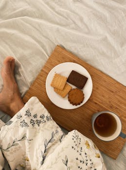 A relaxing morning with tea and cookies served on a wooden board over a cozy, blanket-covered bed.