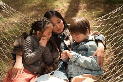 Woman in Denim Shirt Sitting on Hammock with Her Children