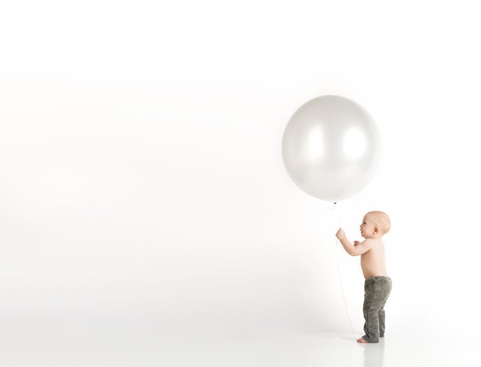 Baby in Black Pants Holding White Balloon While Standing