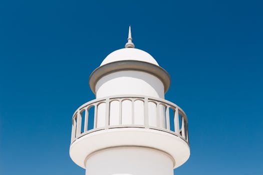 在清澈的蓝天下，矗立着一座极简主义的白色灯塔，展现了现代建筑的风格