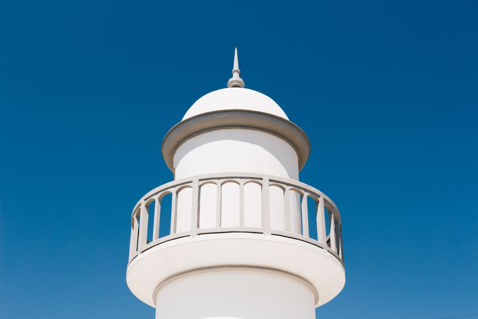 A minimalist white lighthouse tower stands tall against a perfect clear blue sky, showcasing modern architecture.