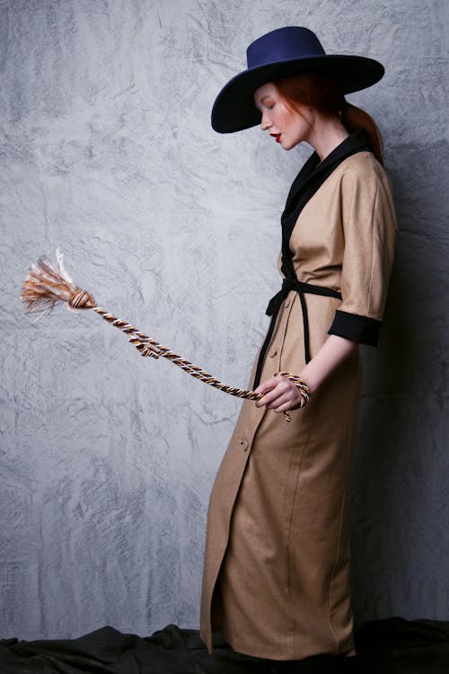 Woman With Ginger Hair and Red Lips Wearing Blue Hat and Beige Robe While Twisting the Rope