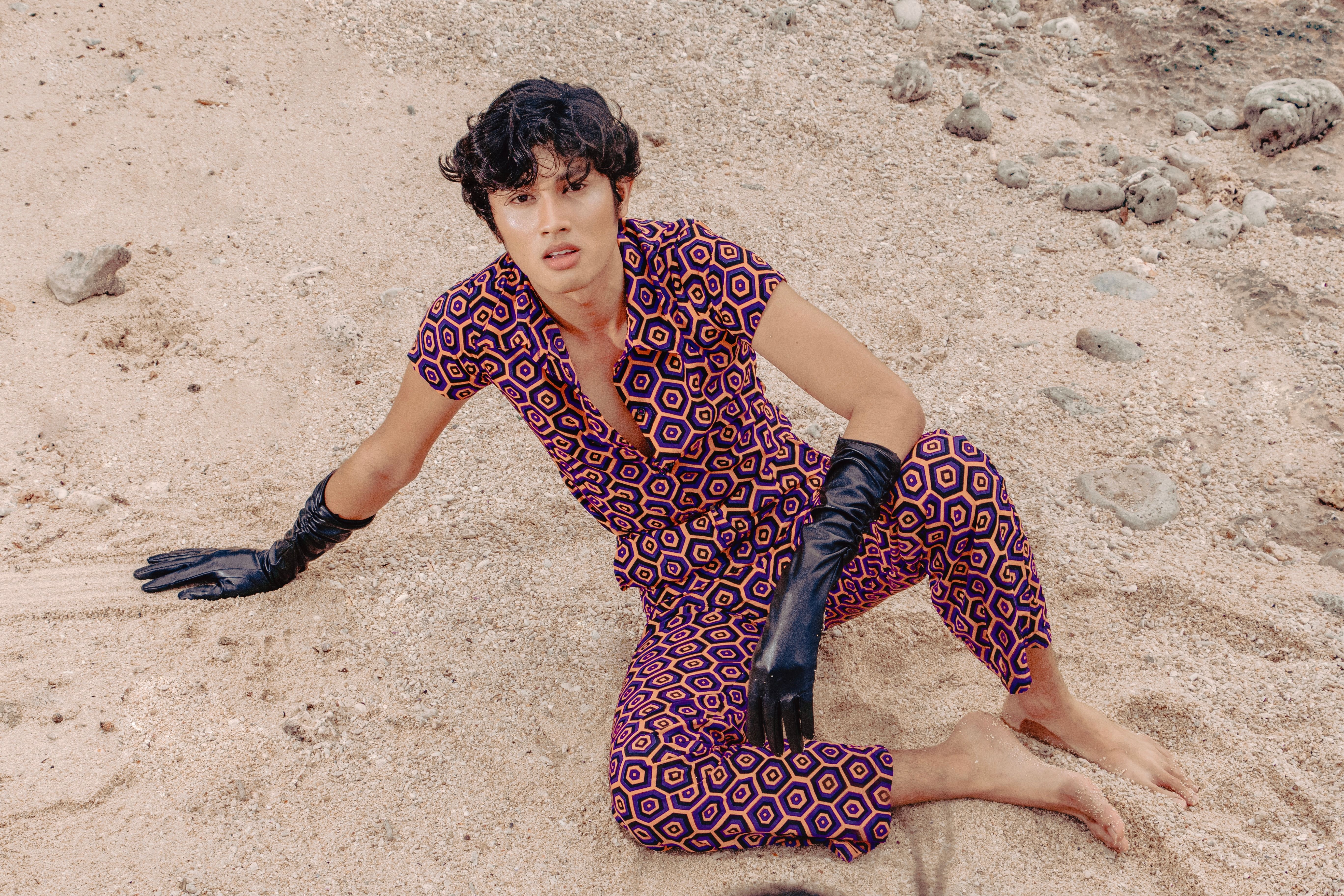 Stylish adult posing outdoors in vibrant patterned outfit with gloves on sandy beach.