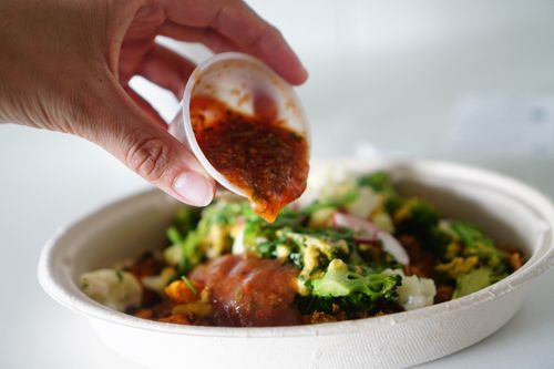 Free Hand pouring salsa over vegetable salad bowl, emphasizing freshness and flavor. Stock Photo