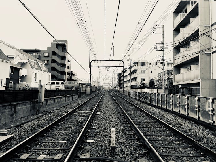 Grayscale Photography Of Train Rail Between Buildings