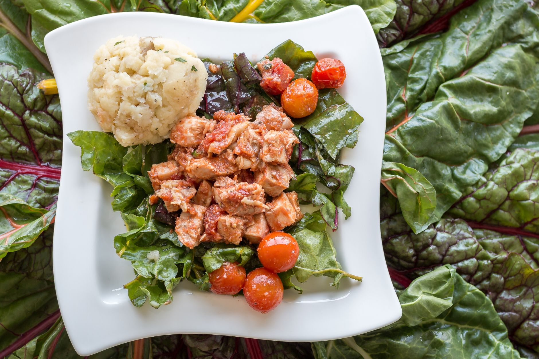 A nutritious dish featuring fish, tomatoes, and greens paired with mashed potatoes served on an elegant plate.