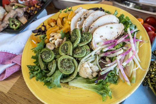 A colorful salad featuring chicken, fiddlehead ferns, and fresh veggies on a yellow plate.