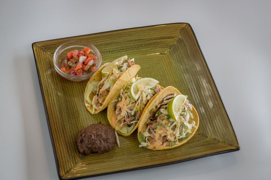 Corn tortillas filled with flaky blackened mahi mahi, shredded purple cabbage slaw, avocado slices, and a drizzle of chipotle crema, arranged on a wooden board with lime wedges.