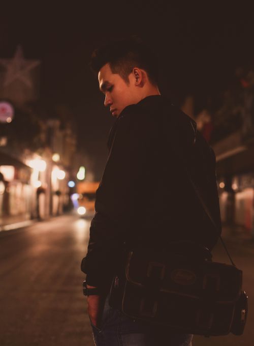 Free Person posing at night in a dimly lit urban street with a messenger bag. Stock Photo