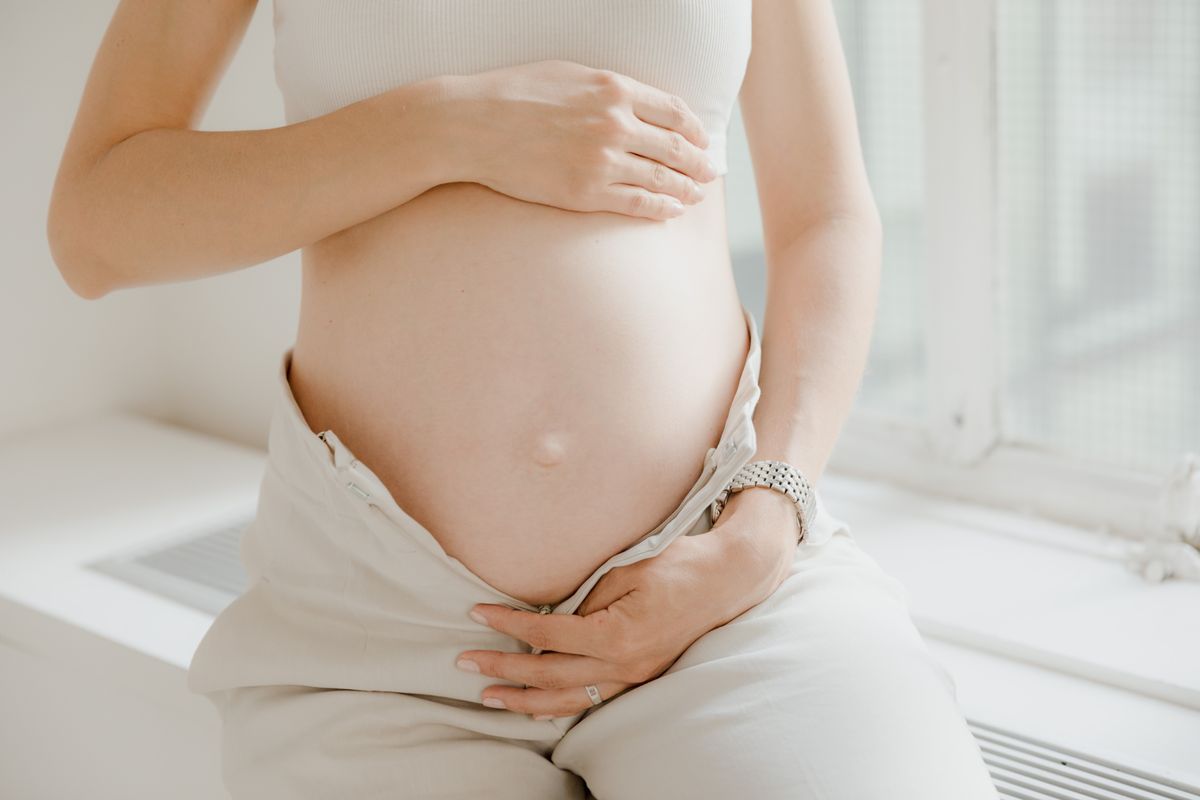 Pregnant woman in white touching her belly